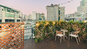 Una terraza en la azotea con suelo de madera, un separador de celosía y un espacio de estar con sillas y una mesa.