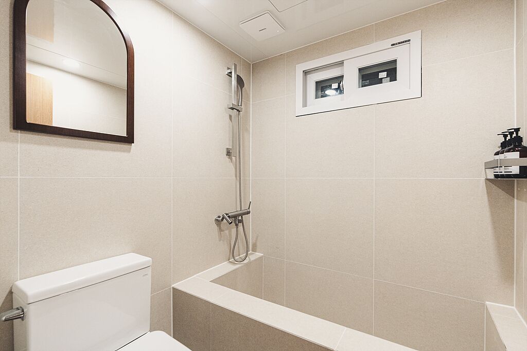 Un baño moderno con inodoro, ducha y una pequeña ventana.