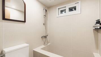 Un baño moderno con inodoro, ducha y una pequeña ventana.