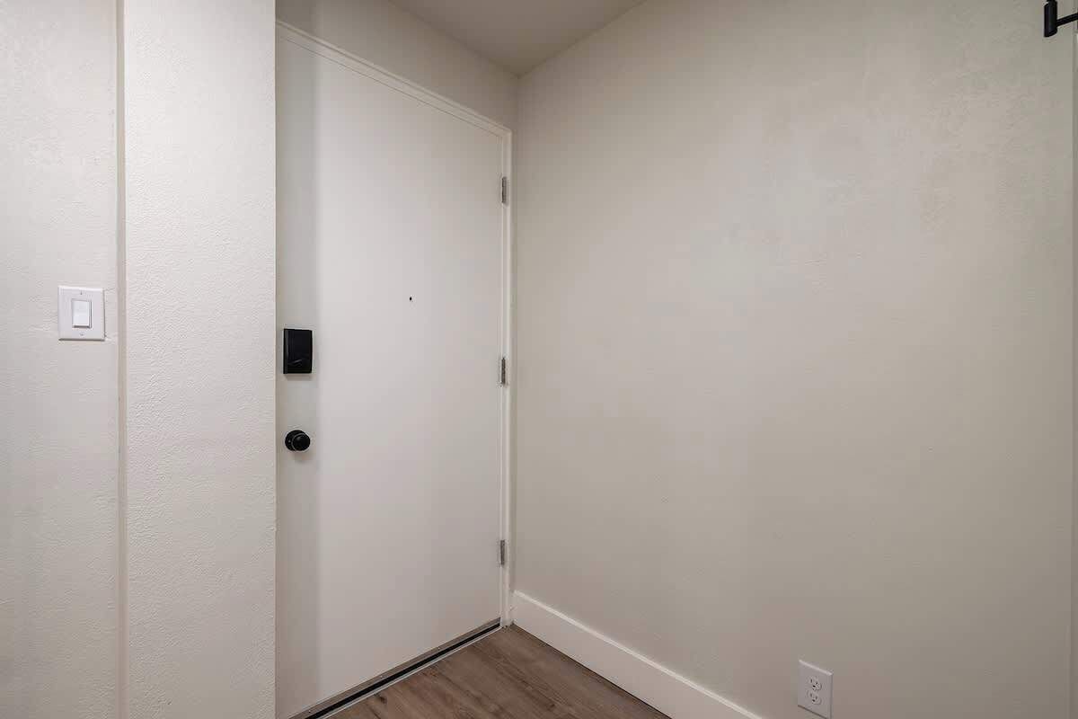 A narrow hallway with a white door, a light switch, and a power outlet on the wall.