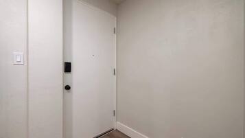 A narrow hallway with a white door, a light switch, and a power outlet on the wall.