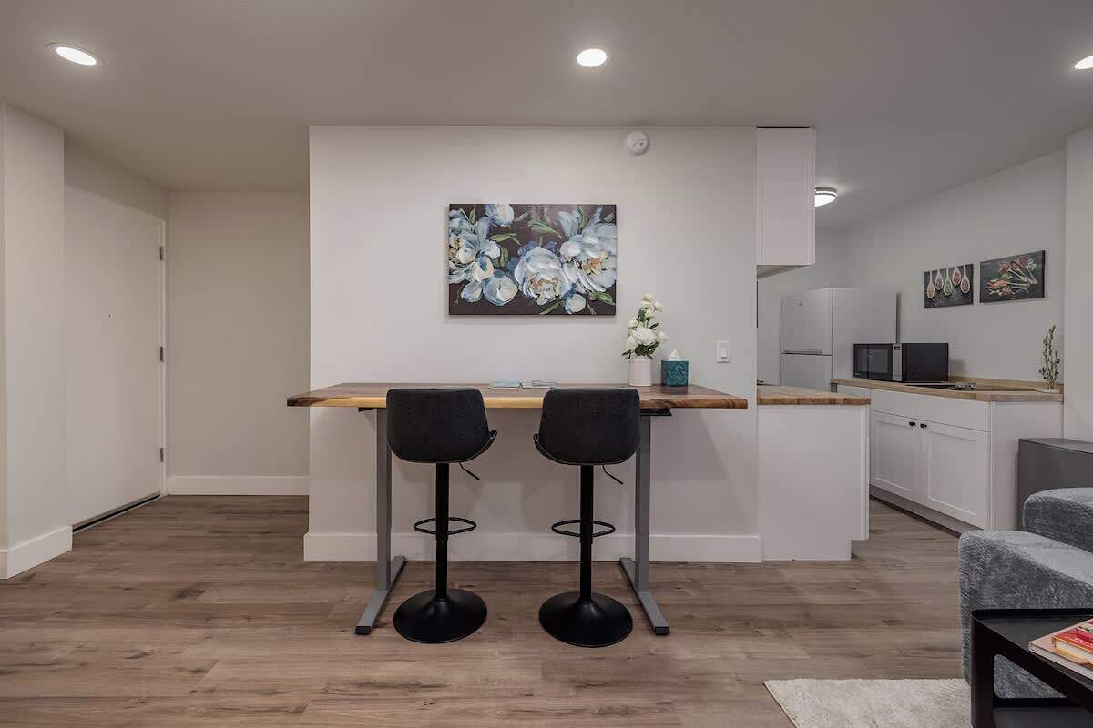 A modern kitchen with white cabinets, a wooden countertop, and two black bar stools.