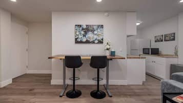 A modern kitchen with white cabinets, a wooden countertop, and two black bar stools.