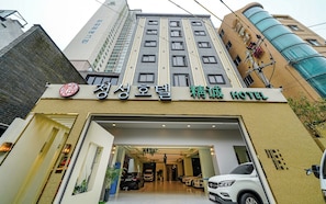 A hotel entrance with a modern design, featuring a large glass facade and a parking area with several cars. - JEONG SEONG HOTEL (Busan)