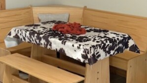 A wooden bed with a patterned bedspread and a red blanket, a wooden bench, and a framed picture on the wall. - The Ranch Luxury Experiences (Gadsden)