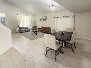 A spacious living area with a dining table, chairs, a sofa, and a chandelier.