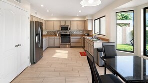 Una cocina moderna con electrodomésticos de acero inoxidable, un comedor con mesa y sillas, y vistas al exterior a través de amplios ventanales.