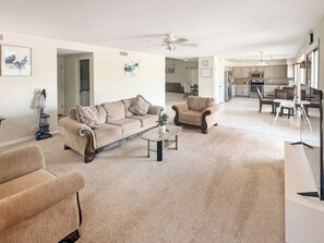 A spacious living room with a beige carpet, a coffee table, and two sofas. There is a kitchen in the background with modern appliances. - 3BR Casa Grande Home with Private Pool and Sofa Sleeper (Casa Grande)