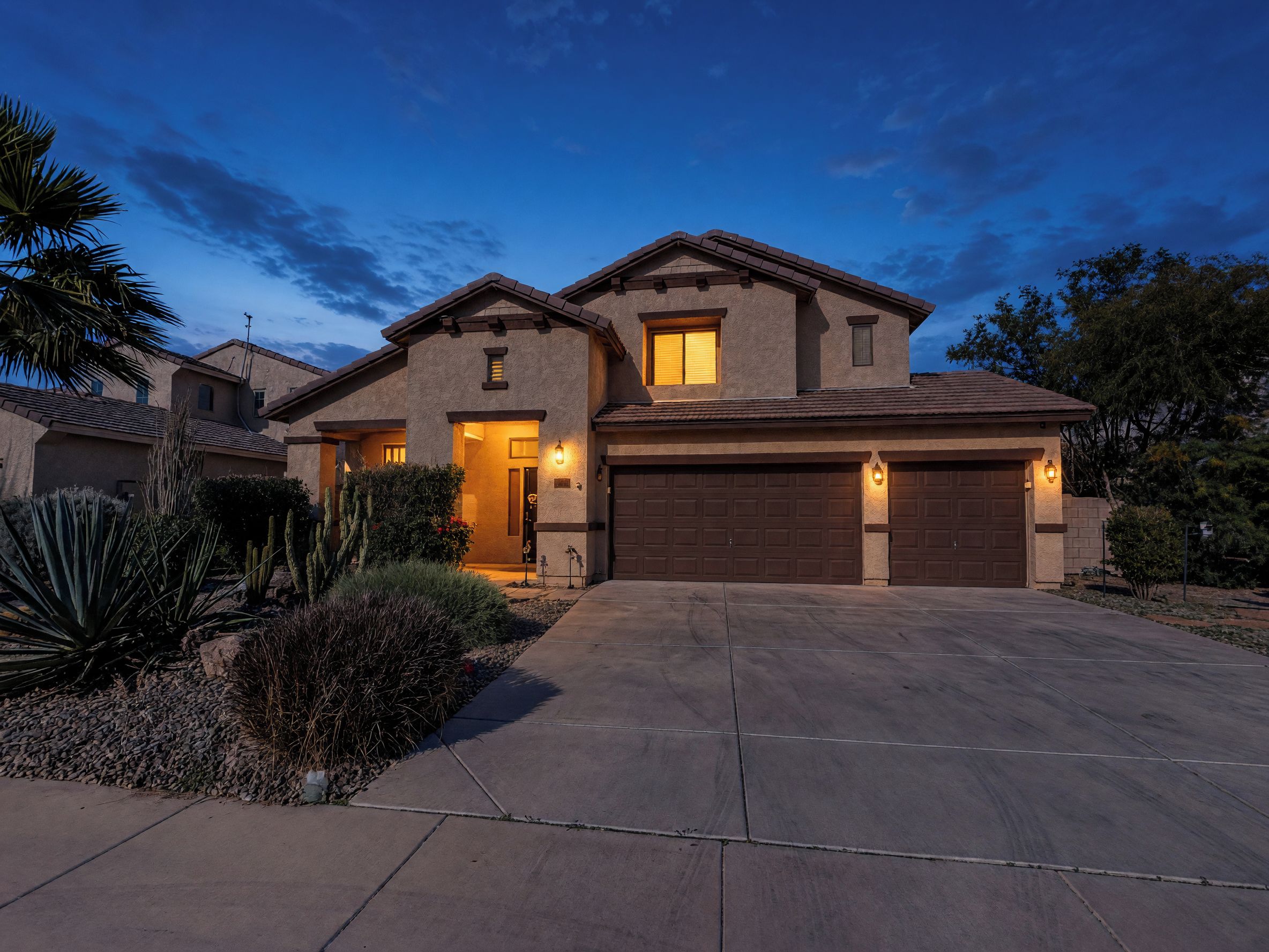A two-story house with a garage, a driveway, and a well-maintained garden with cacti and shrubs.