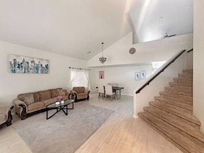 A spacious living room with a sofa, coffee table, and dining area. A staircase leads to an upper level.