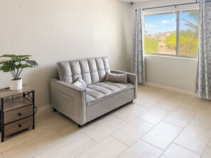 A living room with a grey sofa, a small table with a plant, and a window with curtains. - 3BR Casa Grande Home with Private Pool and Sofa Sleeper (Casa Grande)