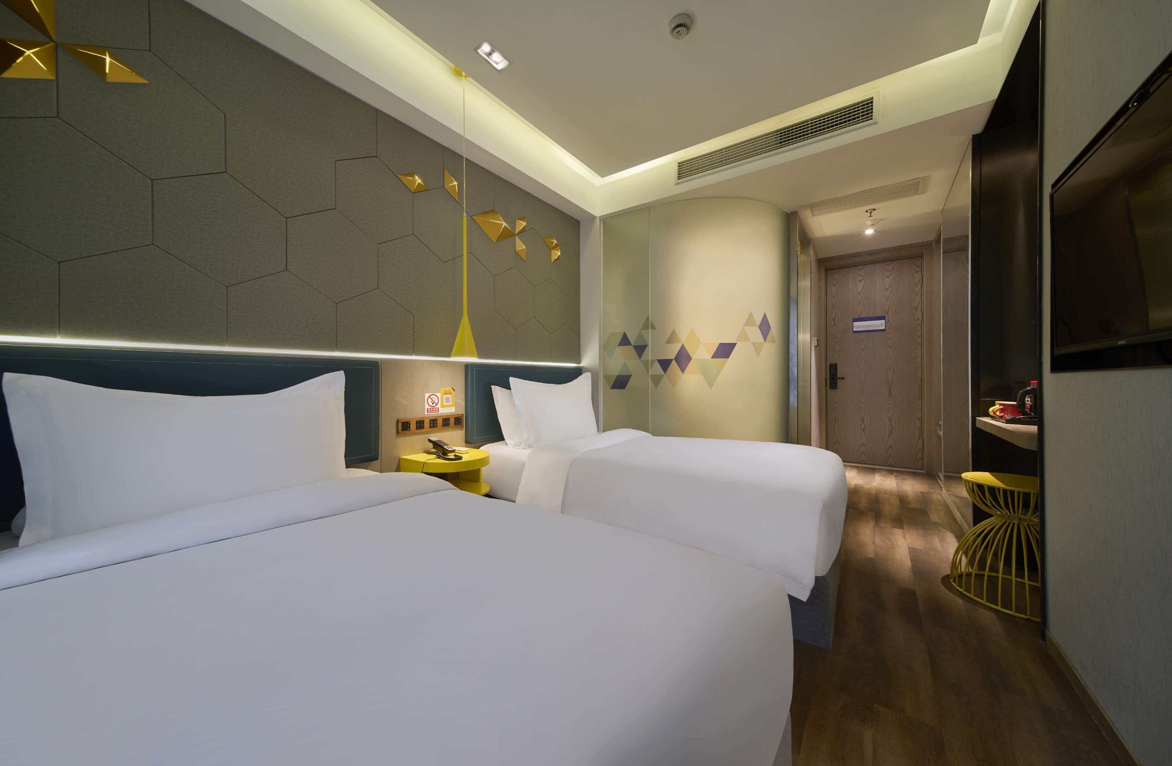A hotel room with two beds, a modern design, a small table with a lamp, and a door leading to a bathroom.
