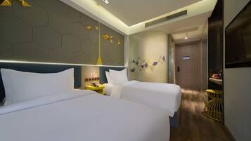 A hotel room with two beds, a modern design, a small table with a lamp, and a door leading to a bathroom.