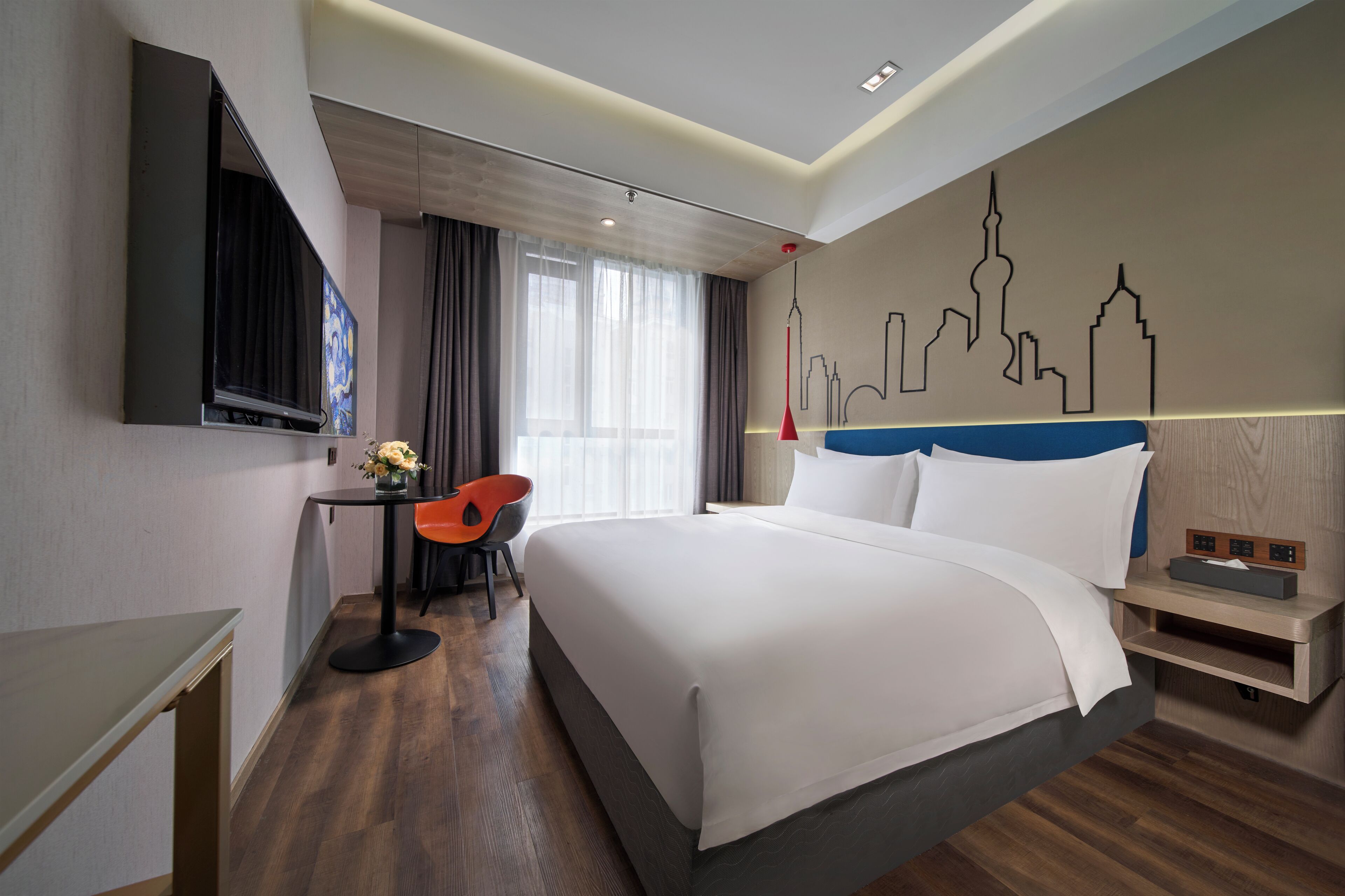 Une chambre d’hôtel moderne avec un grand lit, un bureau avec une chaise, une télévision et une œuvre d’art représentant le panorama de la ville, accrochée au mur.