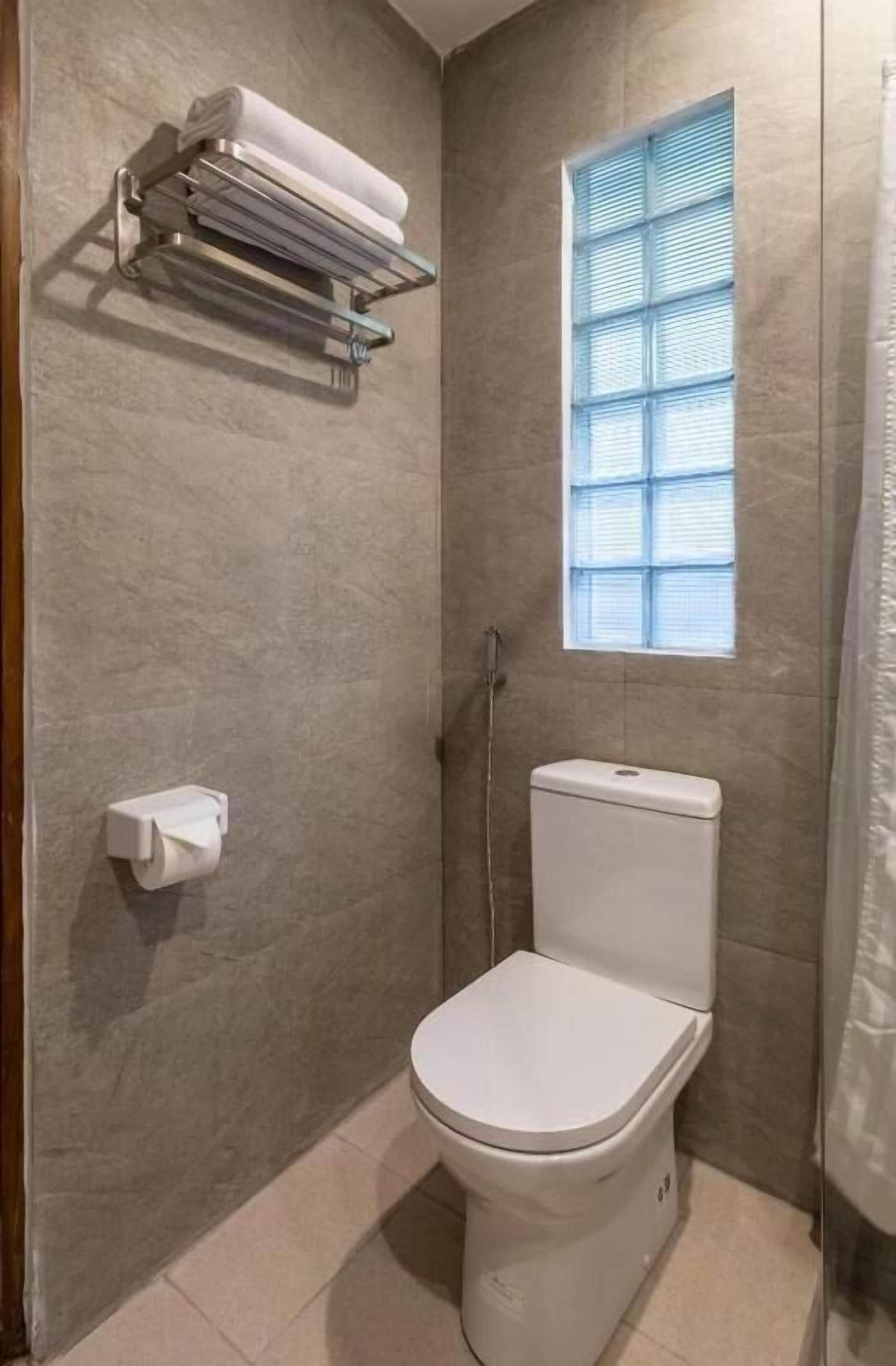 A small, modern bathroom with a toilet, a towel rack, and a window.
