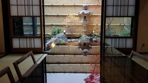Une pièce de style japonais traditionnel, avec un sol recouvert de tatamis, une table basse et une vue sur un bassin en pierre, le tout visible à travers un paravent shoji.