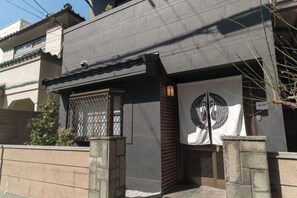 A building with a traditional Japanese architectural style, featuring a tiled roof, a wooden gate, and a stone wall. - KONJAKUSO Osaka Tsuruhashi "KAKUJU" (Osaka)