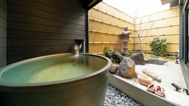 A traditional Japanese onsen with a large hot spring, wooden walls, a bamboo fence, and a stone lantern in the background. - KONJAKUSO Osaka Tsuruhashi "KAKUJU" (Osaka)