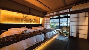 Une pièce de style japonais traditionnel, avec un sol recouvert de tatamis, un lit bas agrémenté de plusieurs oreillers, un paravent shoji et une vue sur la verdure environnante.
