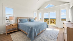 A bedroom with a large bed, a nightstand, a desk, and a view of the ocean. - NEWLY RENOVATED! Oceanfront, Beach Access, Dog Friendly, Spacious Decks (Salvo)