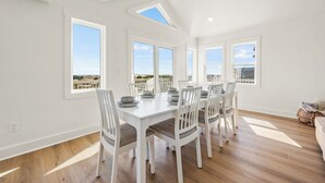A bright dining area with a large table and chairs, large windows with a view, and a skylight. - NEWLY RENOVATED! Oceanfront, Beach Access, Dog Friendly, Spacious Decks (Salvo)