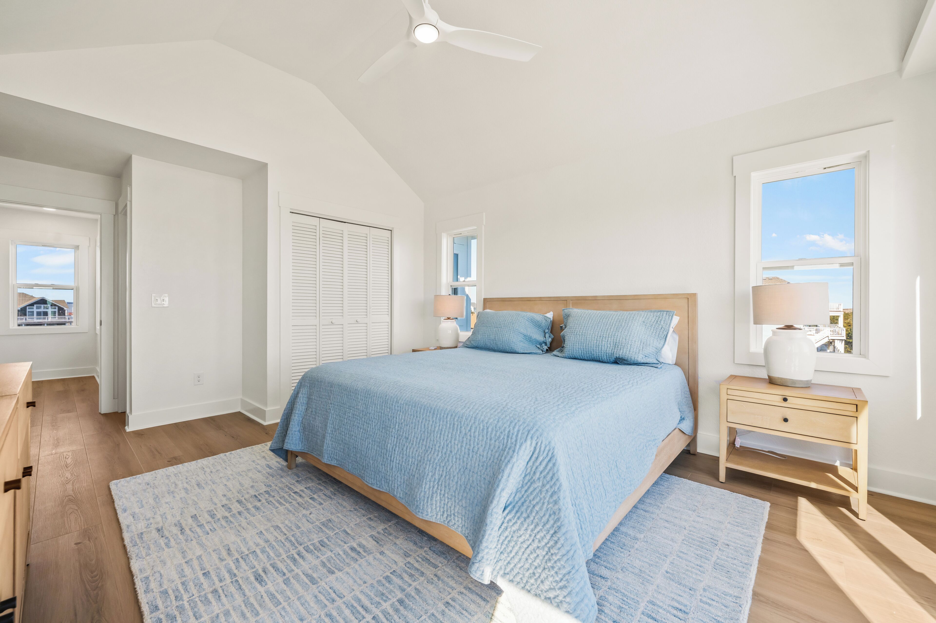 A bedroom with a large bed, a nightstand, a ceiling fan, and a window with a view.