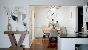 Eine moderne Küche mit Essbereich, ausgestattet mit einem Holztisch, Stühlen, einer großen Wanduhr und einem Deckenventilator.