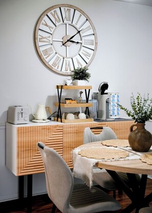 En matplats med ett träbord, stolar, en stor väggklocka och en buffédisk med olika rätter.