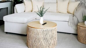 Ein modernes Wohnzimmer mit einem weißen Sofa, einem runden gewebten Couchtisch und einer großen Zimmerpflanze.