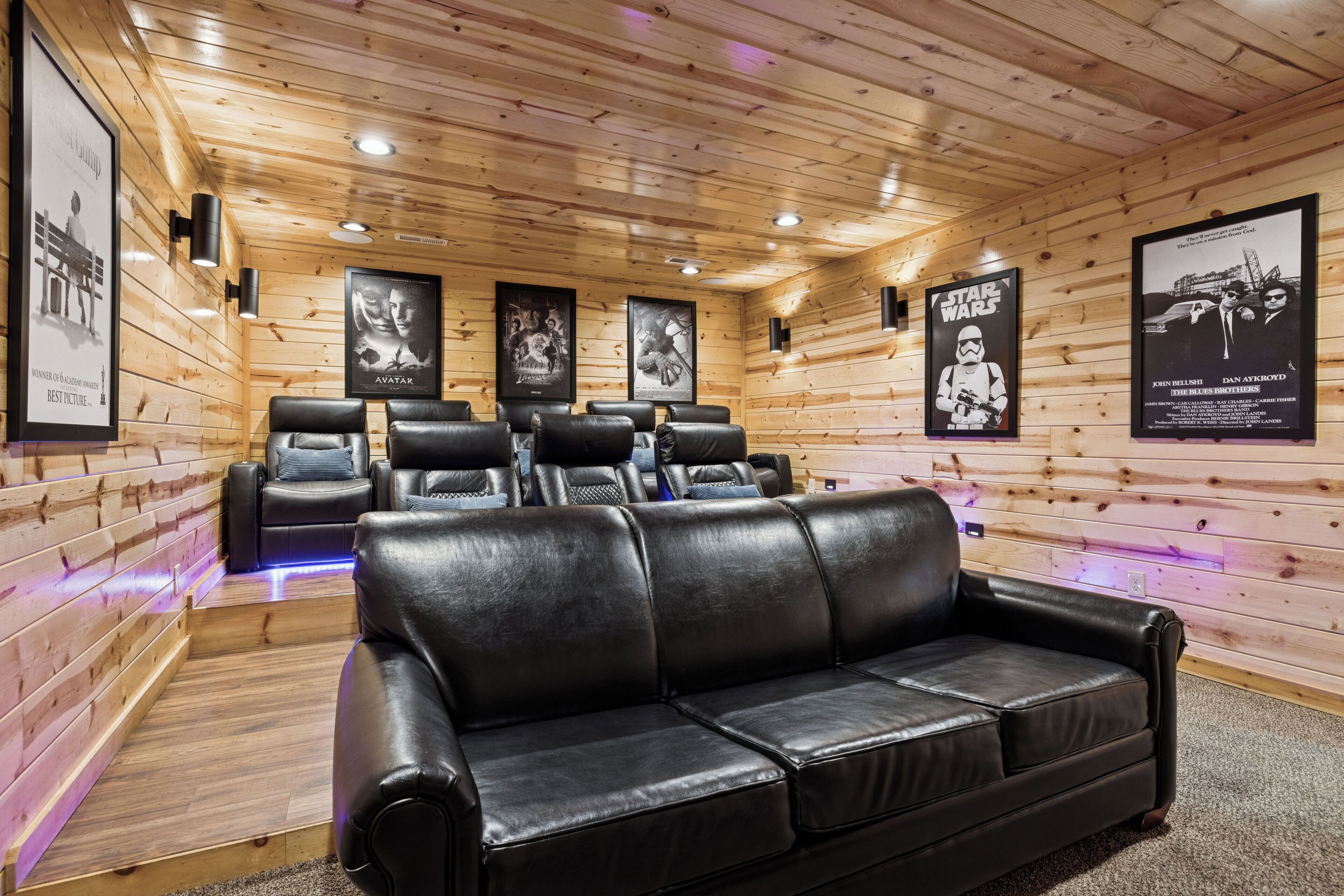 Une pièce chaleureuse aux murs et au plafond en bois, comprenant un canapé en cuir noir et plusieurs fauteuils inclinables.