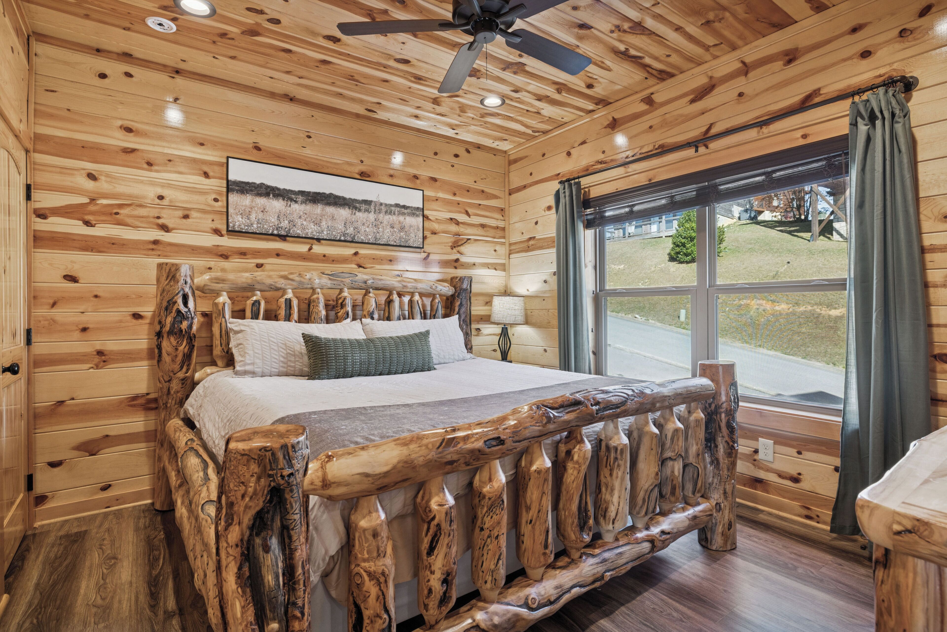 A wooden cabin bedroom with a bed, a ceiling fan, and a window with curtains.