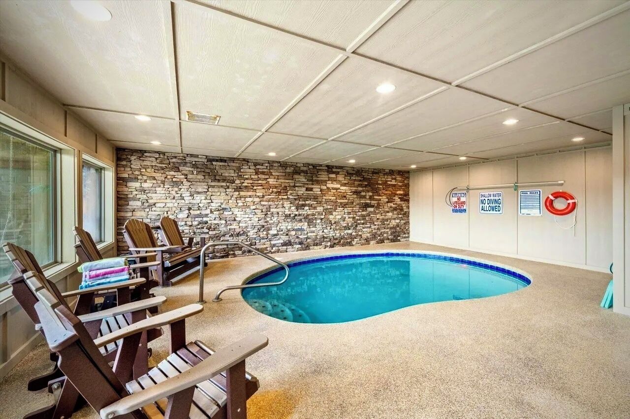 An indoor swimming pool with a stone wall backdrop, lounge chairs, and safety signs.