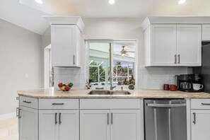 A modern kitchen with white cabinets, a stainless steel sink, and a dishwasher. - Serene Canal Views, Heated Pool & Relaxation - Villa Pelican Paradise - Roelens (Cape Coral)