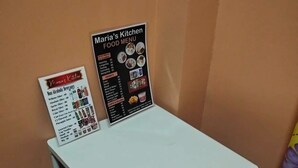 A small table with two black chairs and a menu board for Maria's Kitchen.
