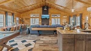 Interior espacioso de una cabaña de madera con comedor, un sofá grande, chimenea y cocina con encimeras de granito.