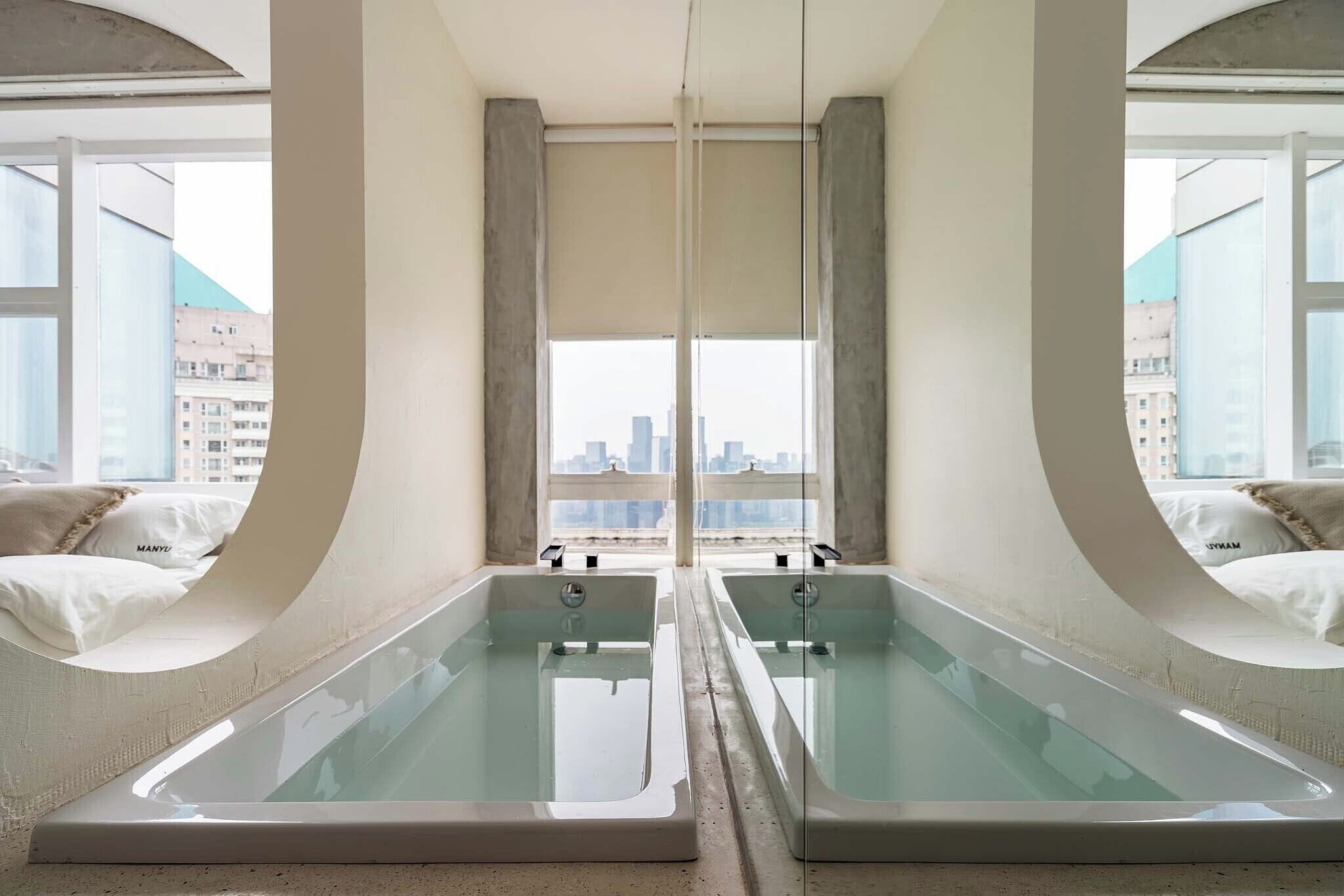 A room with two glass-enclosed tubs, a large window, and a view of the cityscape.