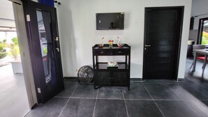 A room with a black door, a small table with decorative items, a fan, and a tiled floor. - Bugbug Beach Resort (Karangasem)