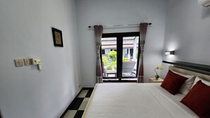 A hotel room with a bed, a nightstand, a wall socket, and a window with curtains. - Bugbug Beach Resort (Karangasem)