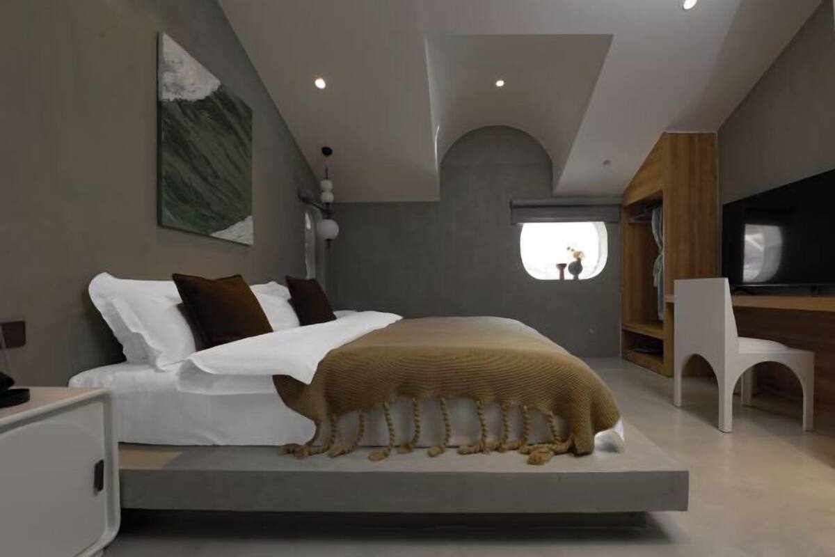 A modern bedroom with a bed, a desk, and a television.