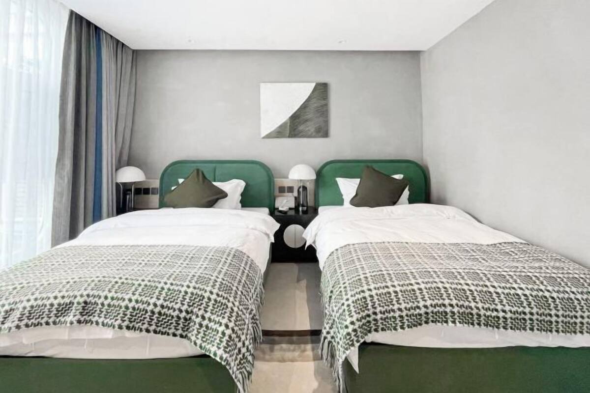 A hotel room with two beds, each with a green headboard, white bedding, and a small bedside table with a lamp.