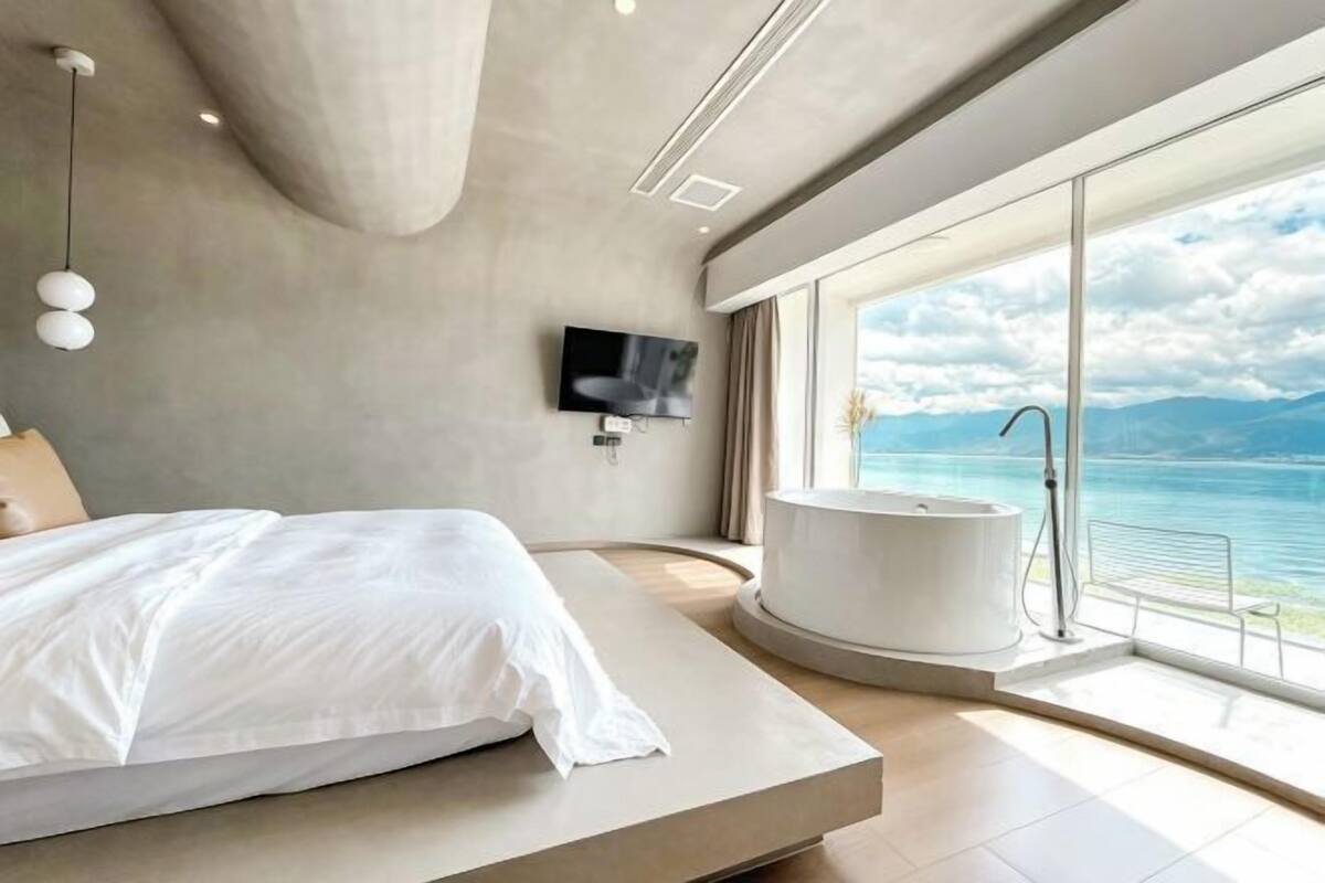 A modern bedroom with a large bed, a bathtub, and a TV.