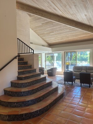 A staircase with patterned steps leading to a living area with a sofa and chairs, a large window, and a ceiling with wooden beams. - Corner fairway & mountain view 3 BR+3.5 BA condo, chef's kitchen, private spa! (Rancho Mirage)