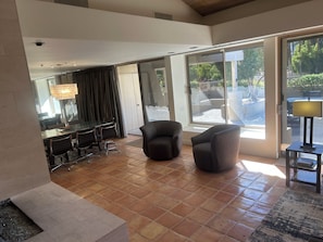 A spacious living area with a glass door leading to an outdoor patio, a dining table with chairs, and a seating area with two armchairs. - Corner fairway & mountain view 3 BR+3.5 BA condo, chef's kitchen, private spa! (Rancho Mirage)