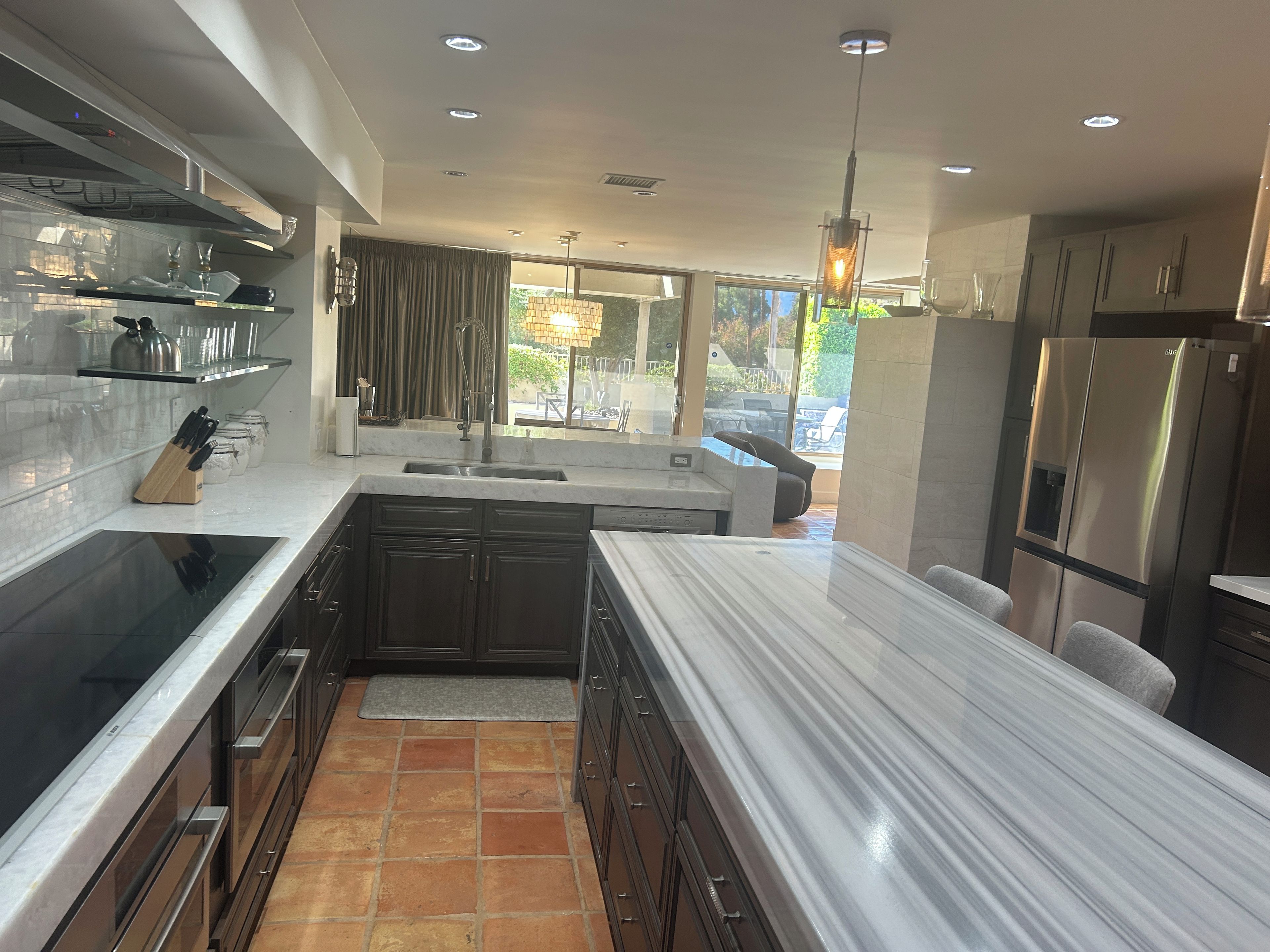 A modern kitchen with dark cabinetry, a stainless steel refrigerator, and a large island with a marble countertop.