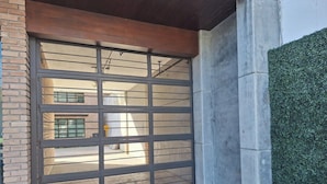 A garage door with a metal grid design, a concrete wall, and a green hedge.