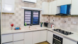 Une cuisine avec des meubles blancs, un four à micro-ondes, une cuisinière à gaz et un four encastré.