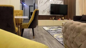 Un salon moderne avec un téléviseur à écran plat fixé à un mur en bois, un canapé jaune, un fauteuil marron et un canapé beige à motifs capitonnés.