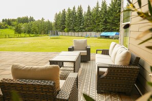 Ein Terrassenbereich im Freien mit Korbmöbeln, einem weißen Sofa und einem gemusterten Teppich.