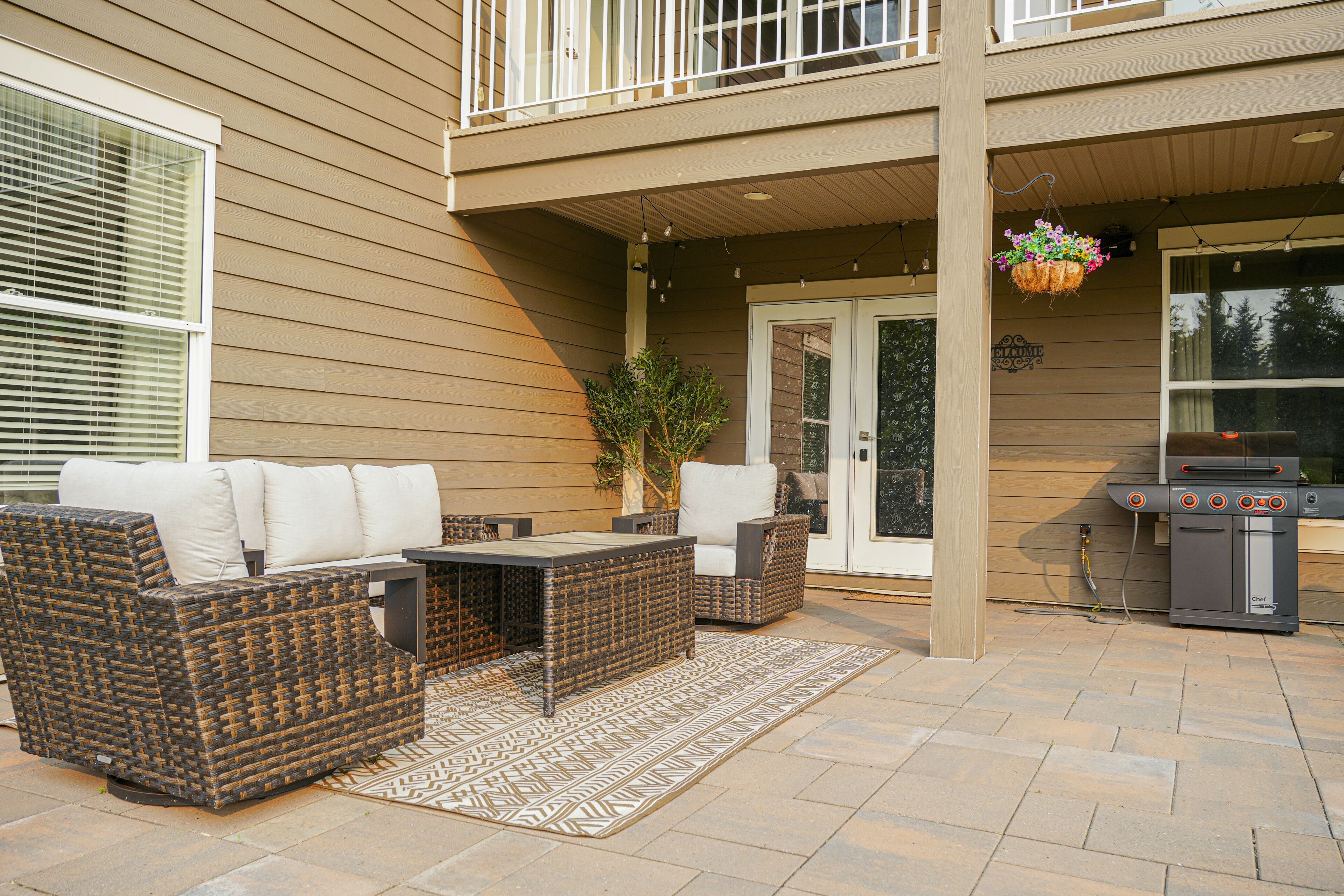 An outdoor patio with wicker furniture, a grill, and a hanging planter.