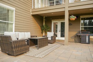 Un patio exterior con mobiliario de mimbre, una parrilla y una maceta colgante.